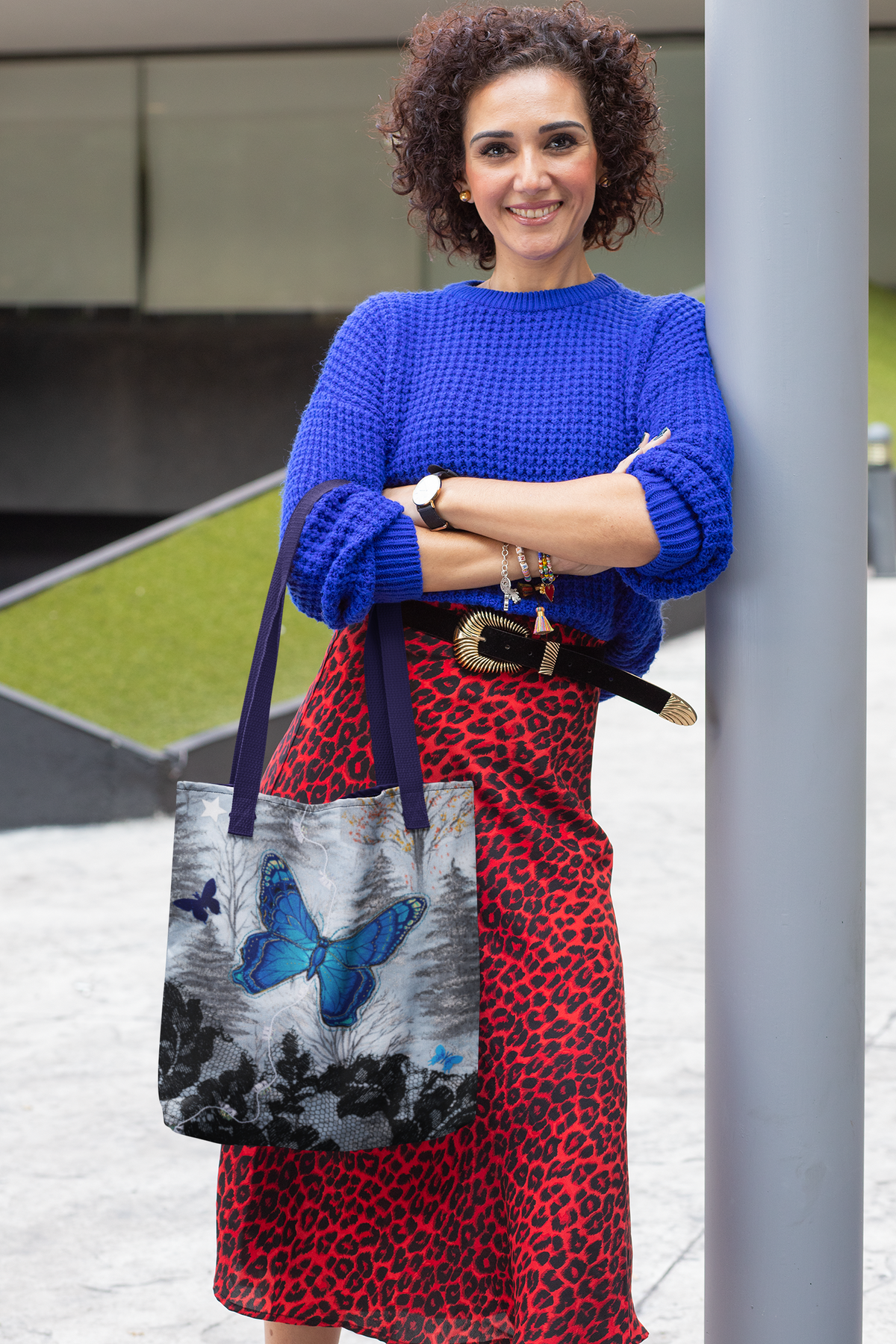 Woman in blue sweater and red leopard print skirt holding a tote bag with  blue butterfly design.